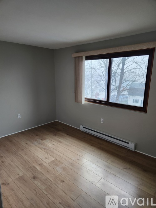 A room with wooden flooring and a window showing a view of a residential area.