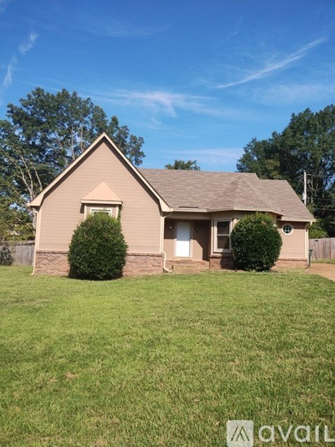 A house with a brown roof and a white door is surrounded by a green lawn.
