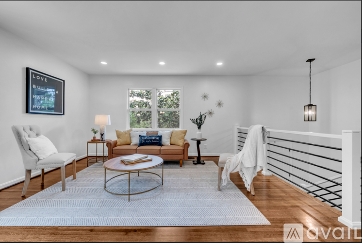 A living room with a white chair, a sofa, a coffee table, and a painting on the wall.