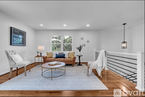 A living room with a white chair, a sofa, a coffee table, and a painting on the wall.