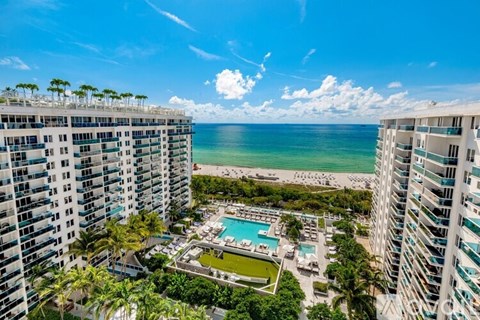 A view of a pool area from a high-rise building with palm trees and a beach in the background.