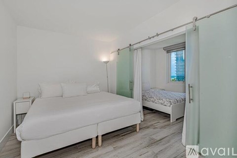 A bedroom with a white bed and a small nightstand.