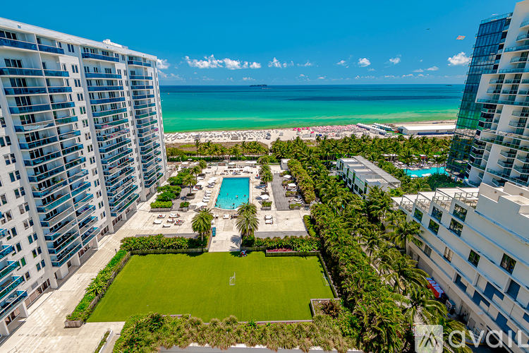 A view of a beachfront property with a swimming pool and a green lawn.
