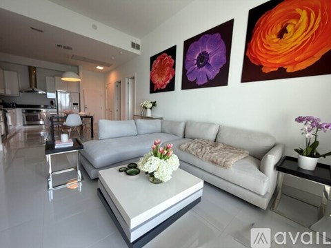 A modern living room with a grey sofa, a coffee table, and three colorful paintings on the wall.