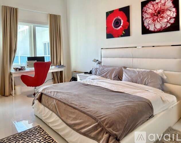 A bedroom with a large bed, a red chair, and two paintings on the wall.