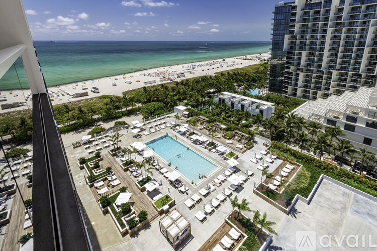 A view from a high-rise building overlooking a pool area with a beach in the distance.