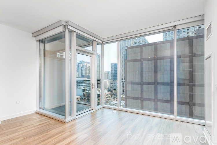 A room with a wooden floor and a glass door leading to a balcony with a city view.