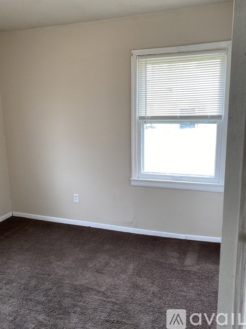 A room with a carpeted floor and a window with blinds.