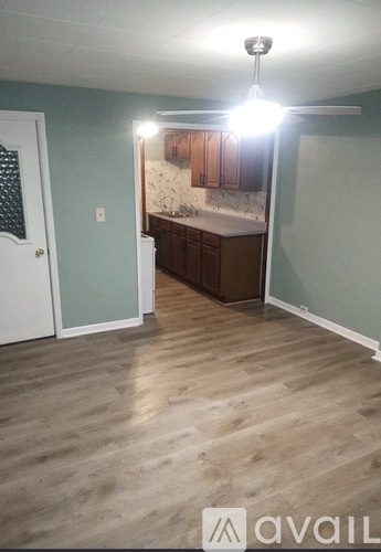 A room with wooden flooring and a kitchen area in the background.