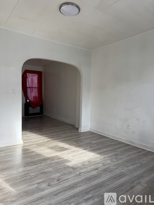 A room with a wooden floor and a white wall with a red door.