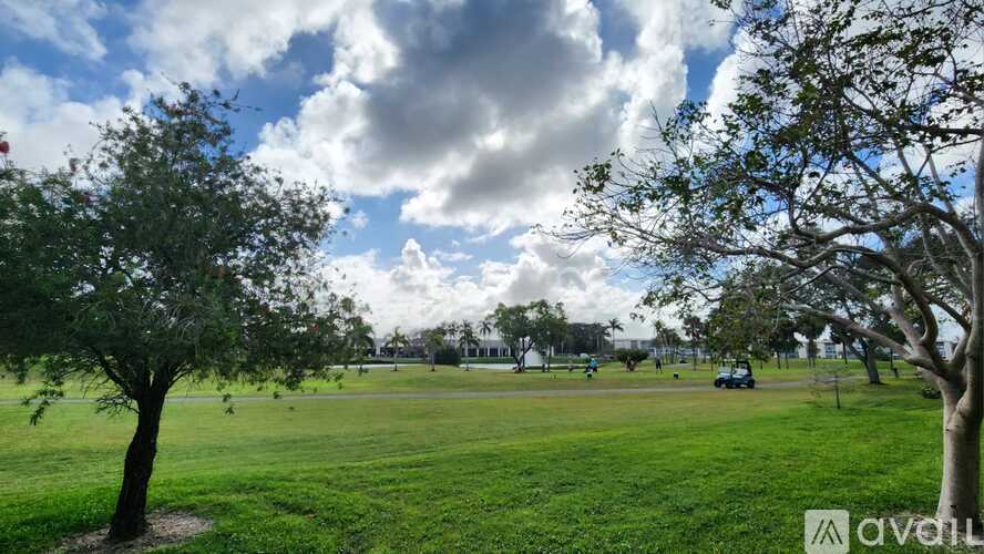 A park with a green lawn and trees under a cloudy sky.