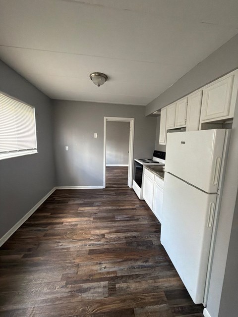 A kitchen with a white fridge and wooden floors.
