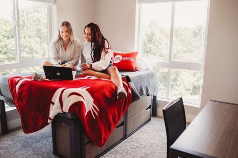 Two people sitting on a bed with a laptop.