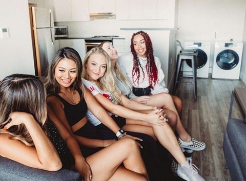 Five women are sitting on a couch in a living room.