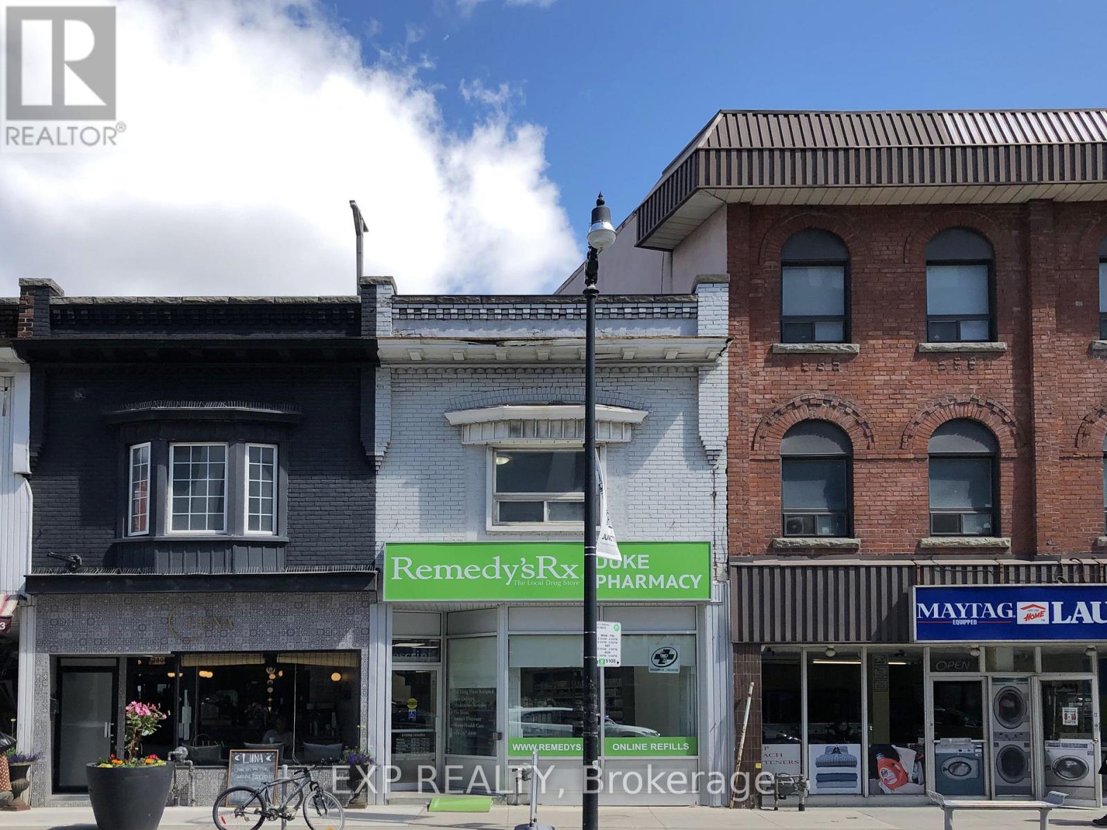 A street view with a pharmacy and a realtor sign.