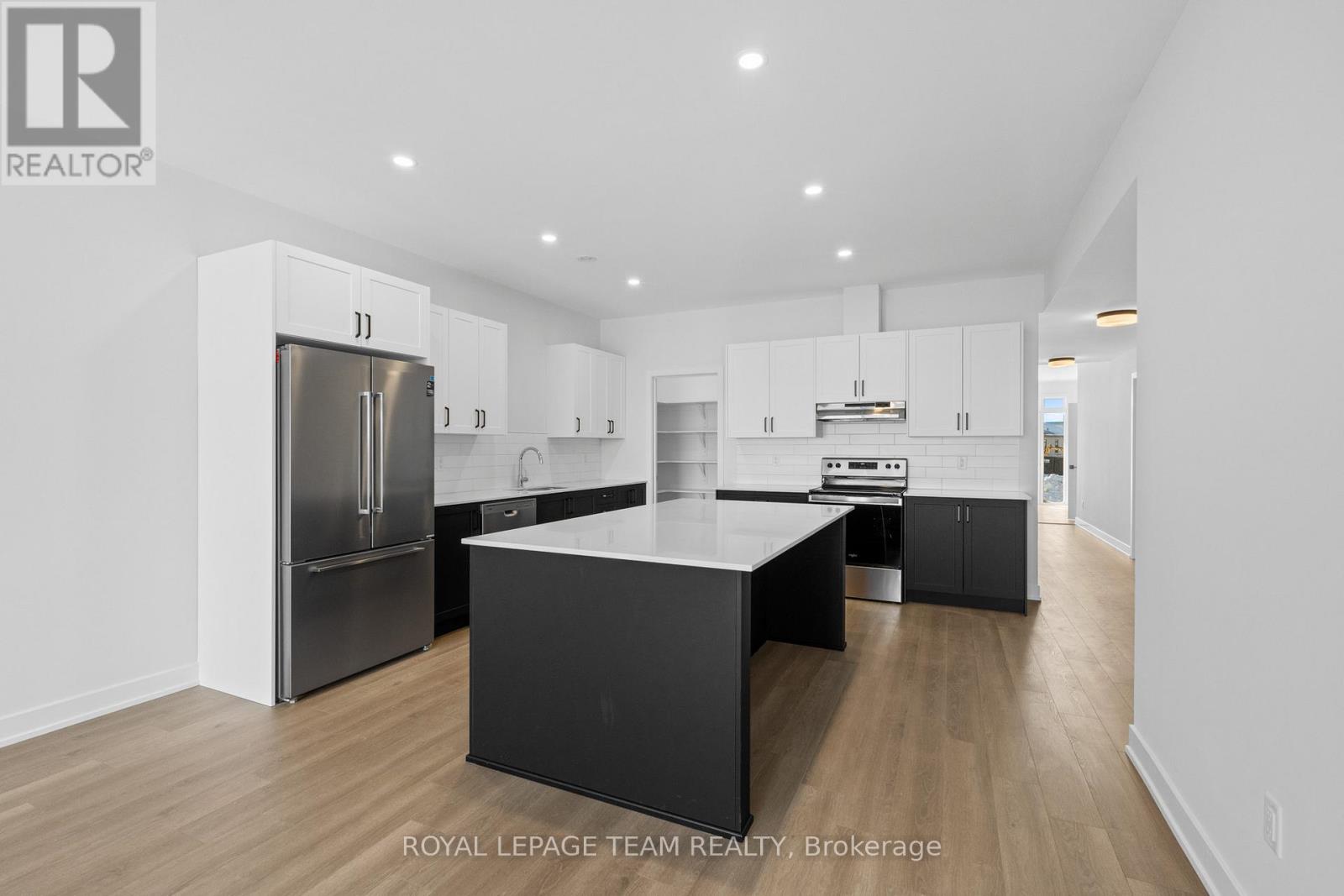 A spacious room with wooden flooring and a large window overlooking a wooden fence.