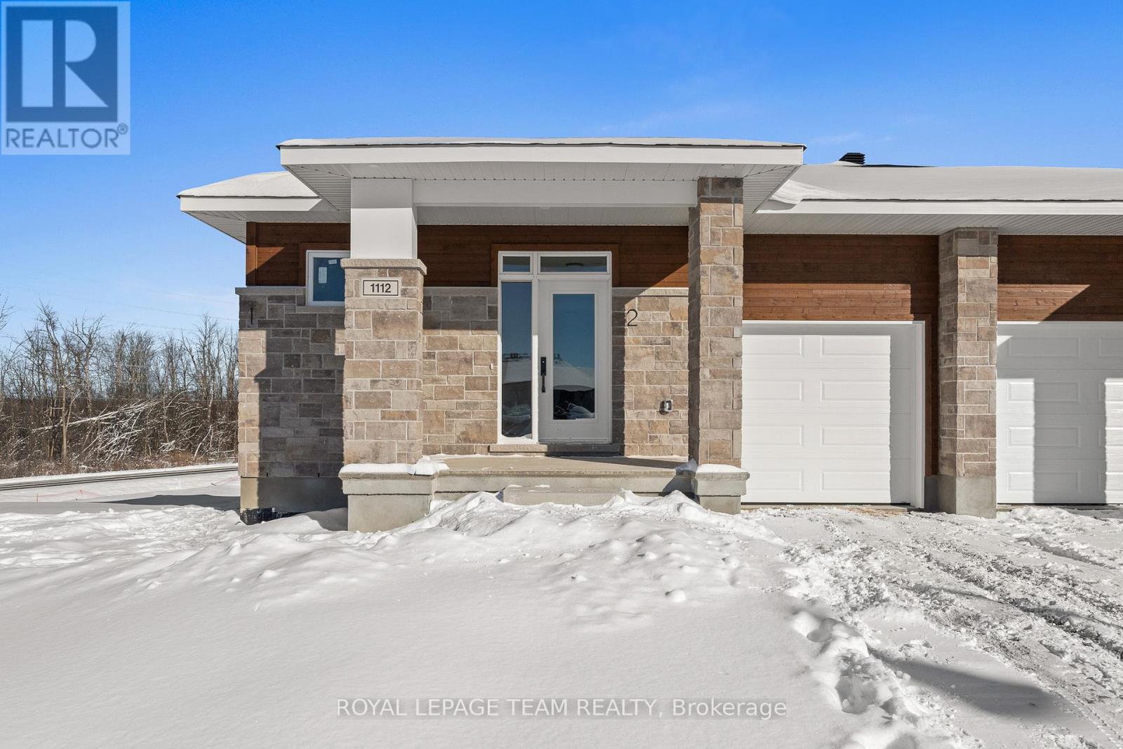 A house with a white garage door and a blue door is surrounded by snow.