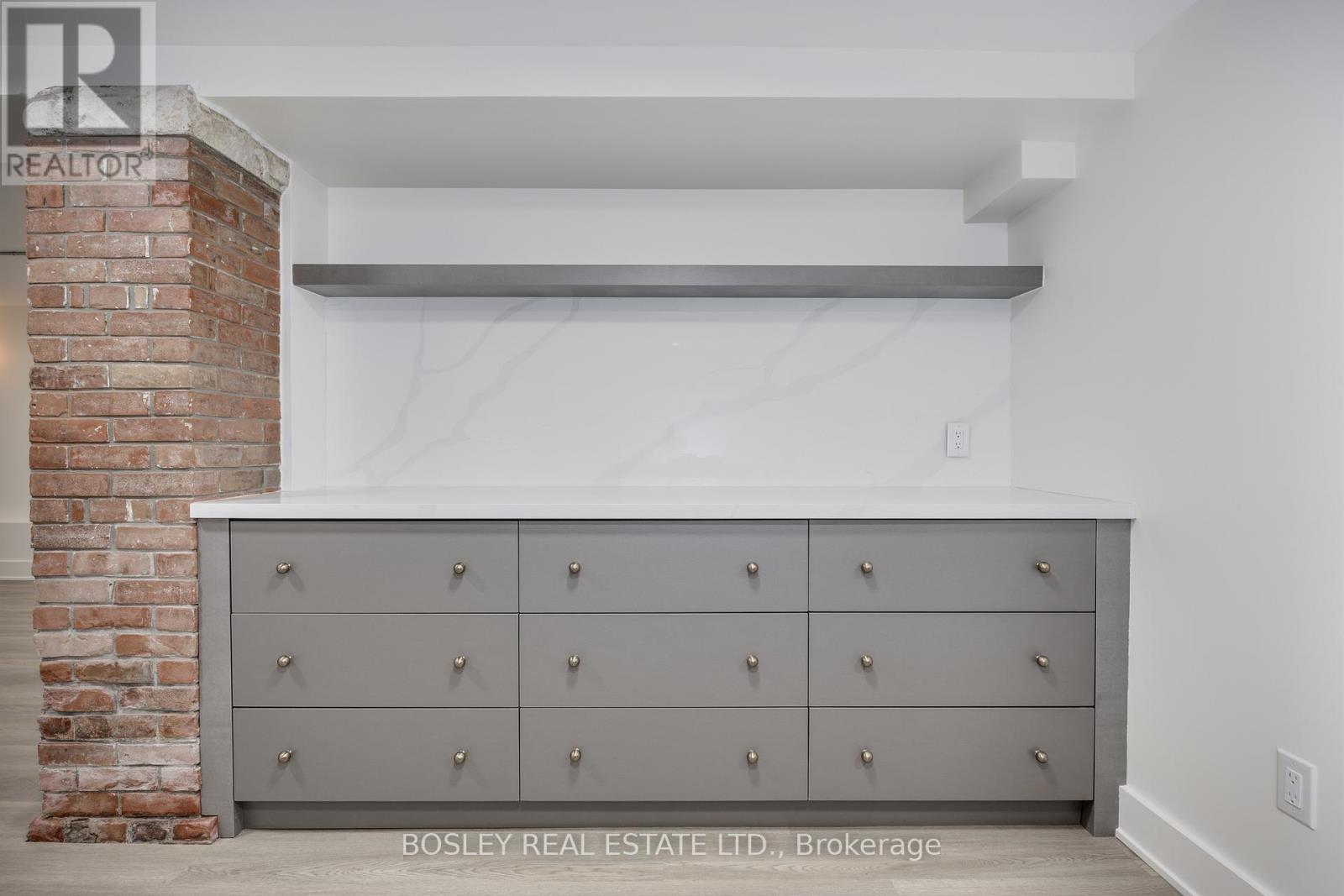 A large grey cabinet with silver knobs is in the foreground of a room with a brick column in the background.