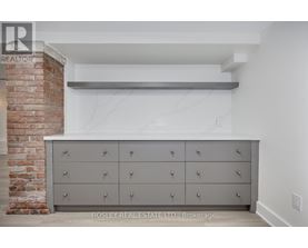 A large grey cabinet with silver knobs is in the foreground of a room with a brick column in the background.