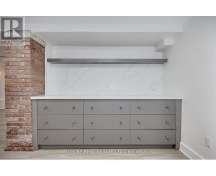 A large grey cabinet with silver knobs is in the foreground of a room with a brick column in the background.