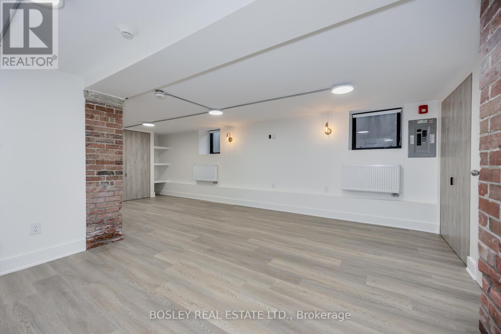A spacious room with wooden flooring and a brick wall on one side.