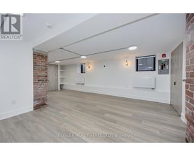 A spacious room with wooden flooring and a brick wall on one side.