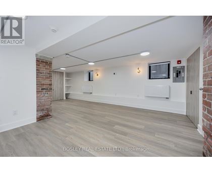 A spacious room with wooden flooring and a brick wall on one side.