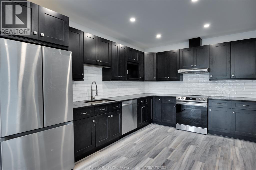 A kitchen with black cabinets and a stainless steel refrigerator.