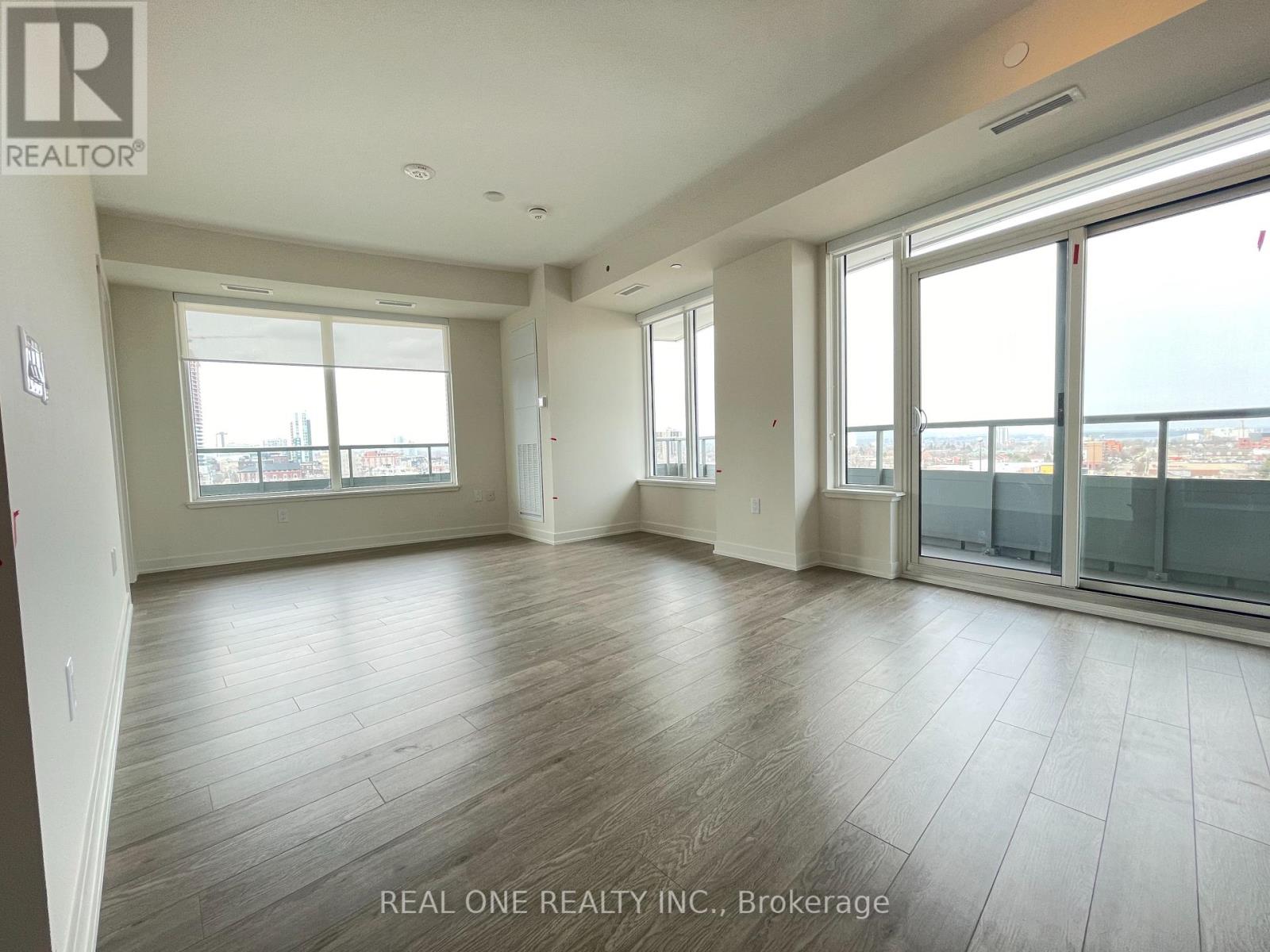 A spacious room with wooden flooring and large windows.