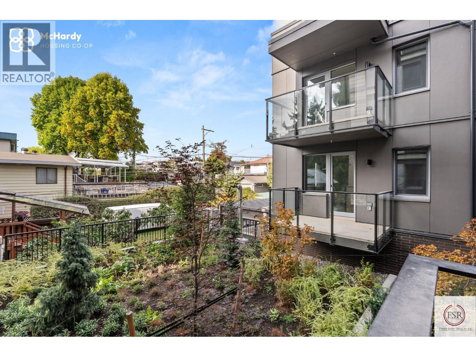 A modern apartment building with a balcony and a garden in front.