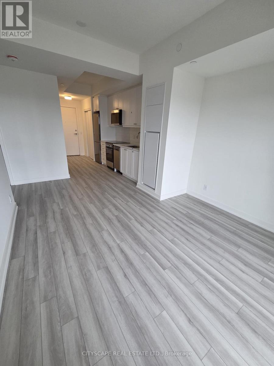 A real estate listing photo of a large empty room with wood flooring and white walls.