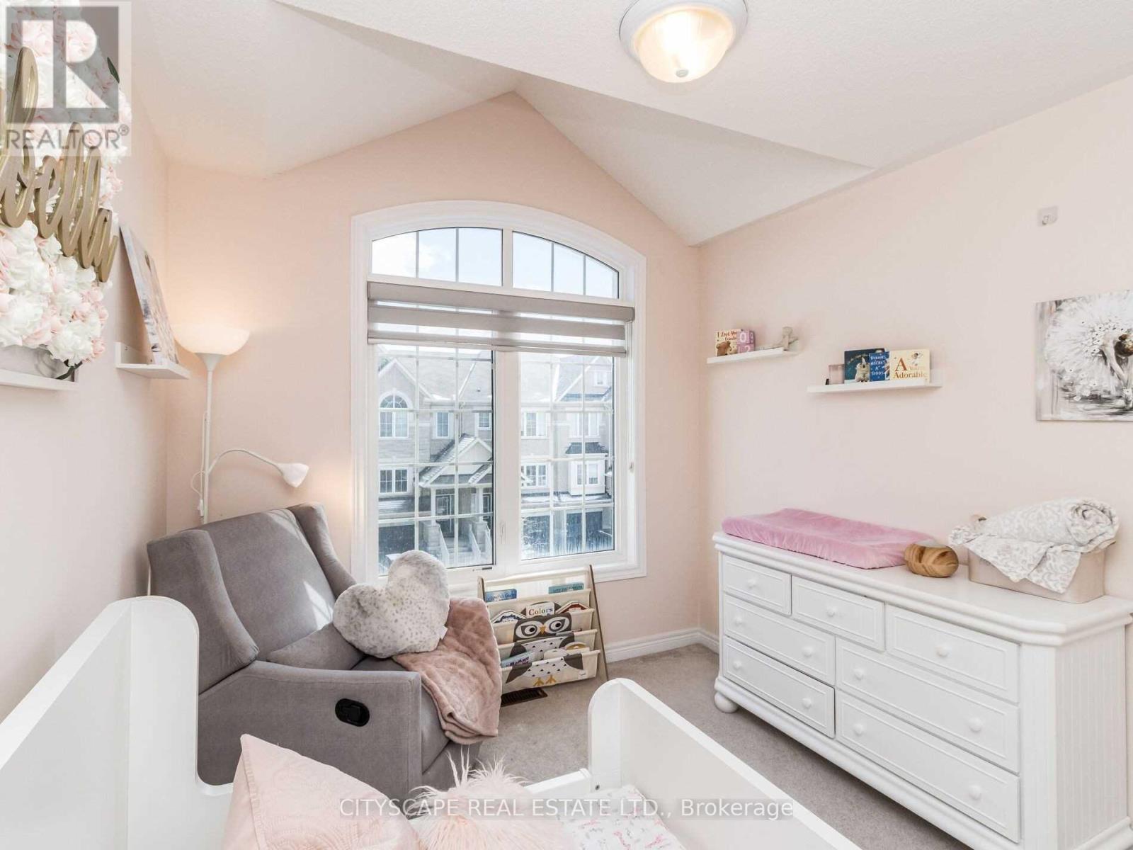 A baby's room with a grey sofa, a white crib, and a window with a view of a building outside.
