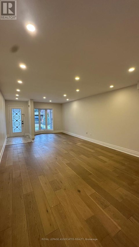 A spacious room with wooden flooring and recessed lighting.