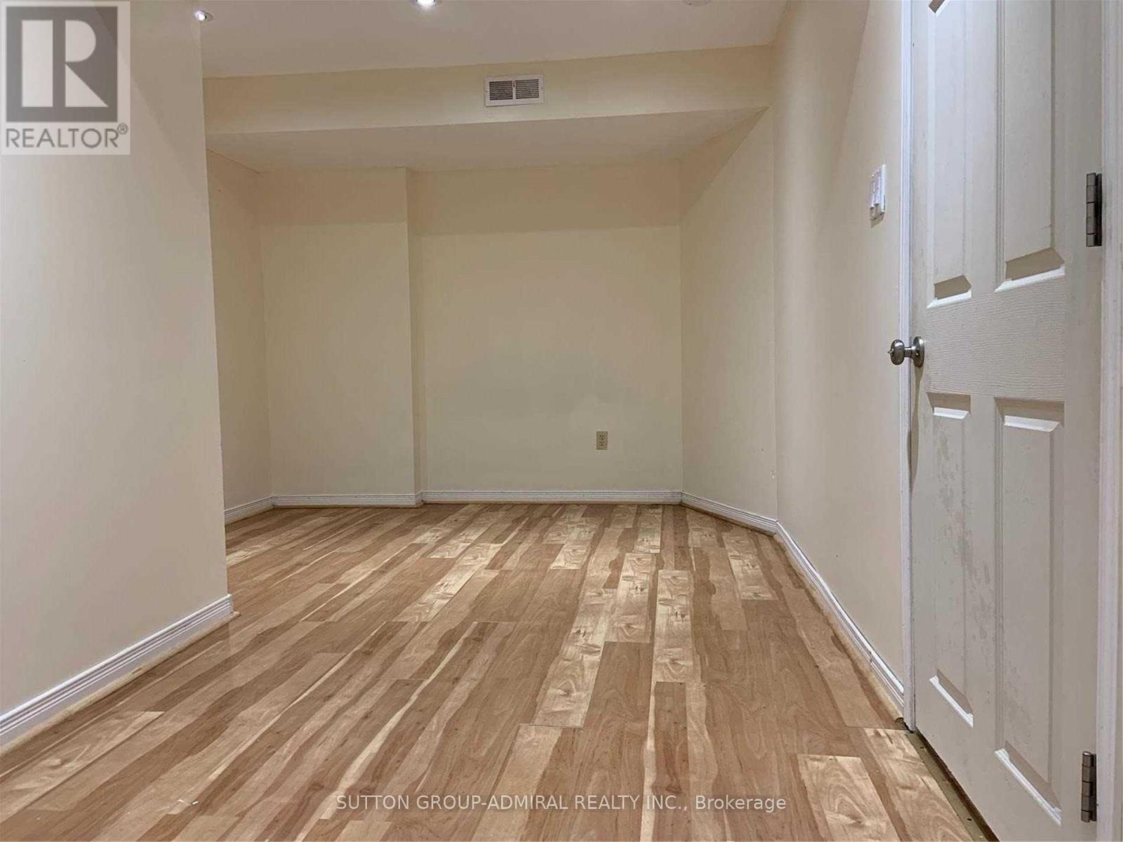 A room with wooden flooring and white walls, with a door on the right side.