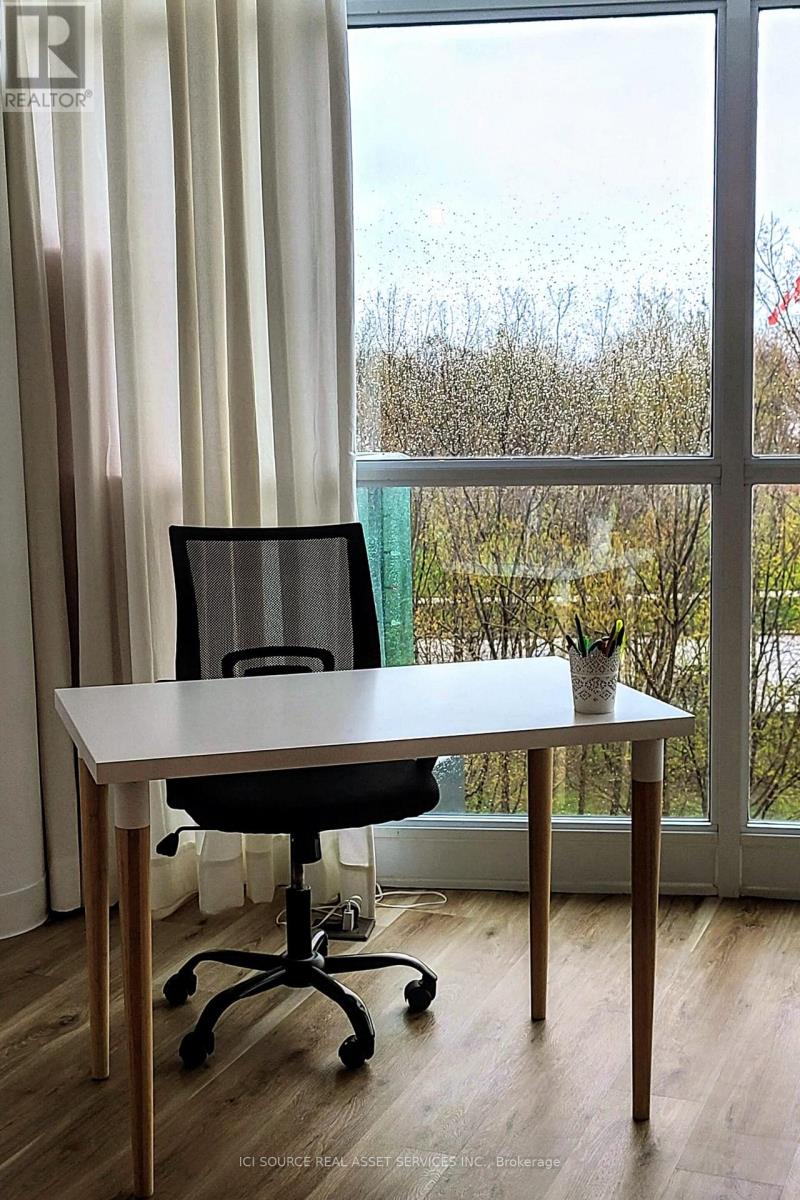 A white desk with a black chair in front of a window with a view of trees outside.