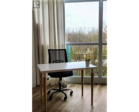 A white desk with a black chair in front of a window with a view of trees outside.