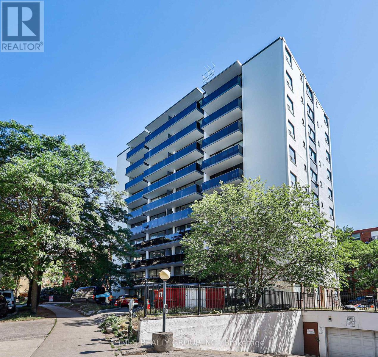 A tall building with a blue and white facade is surrounded by trees and a clear sky.