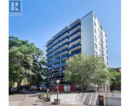 A tall building with a blue and white facade is surrounded by trees and a clear sky.