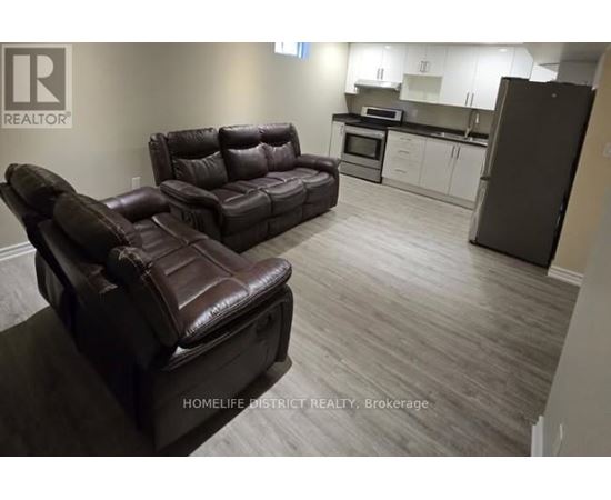 A living room with a brown leather couch and a kitchen area in the background.