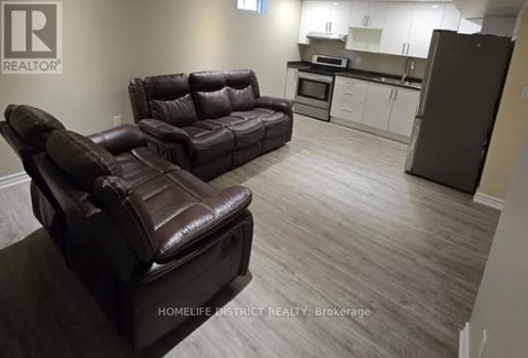 A living room with a brown leather couch and a kitchen area in the background.