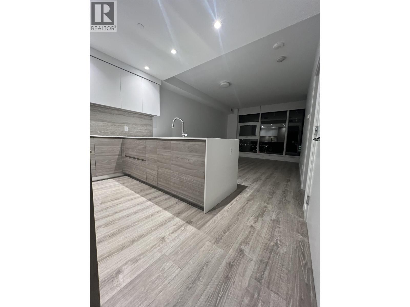 A modern kitchen with wooden flooring and white cabinetry.