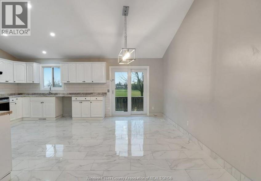 A spacious kitchen with white cabinets and marble flooring.