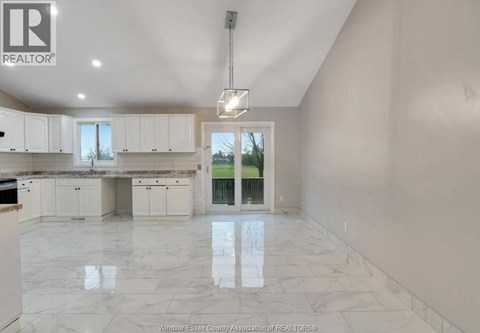 A spacious kitchen with white cabinets and marble flooring.