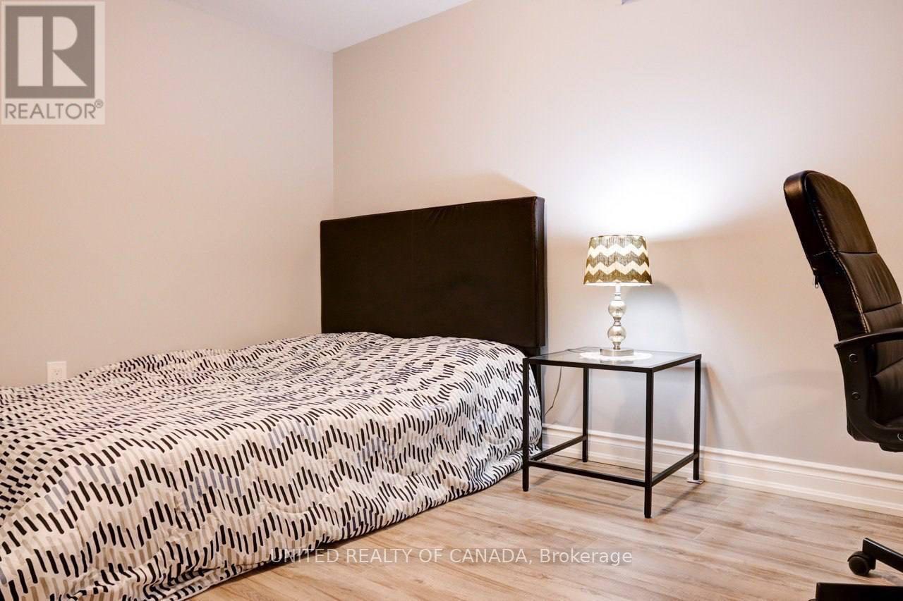 A bedroom with a patterned bedspread, a black headboard, a side table with a lamp, and a black chair.