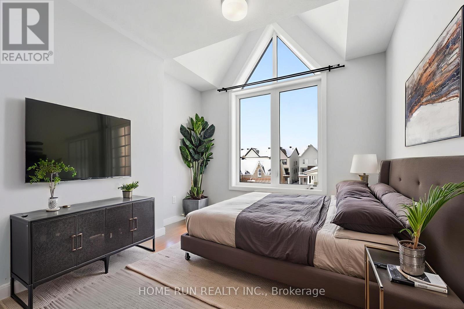 A bedroom with a large bed, a dresser, and a window overlooking a neighborhood.