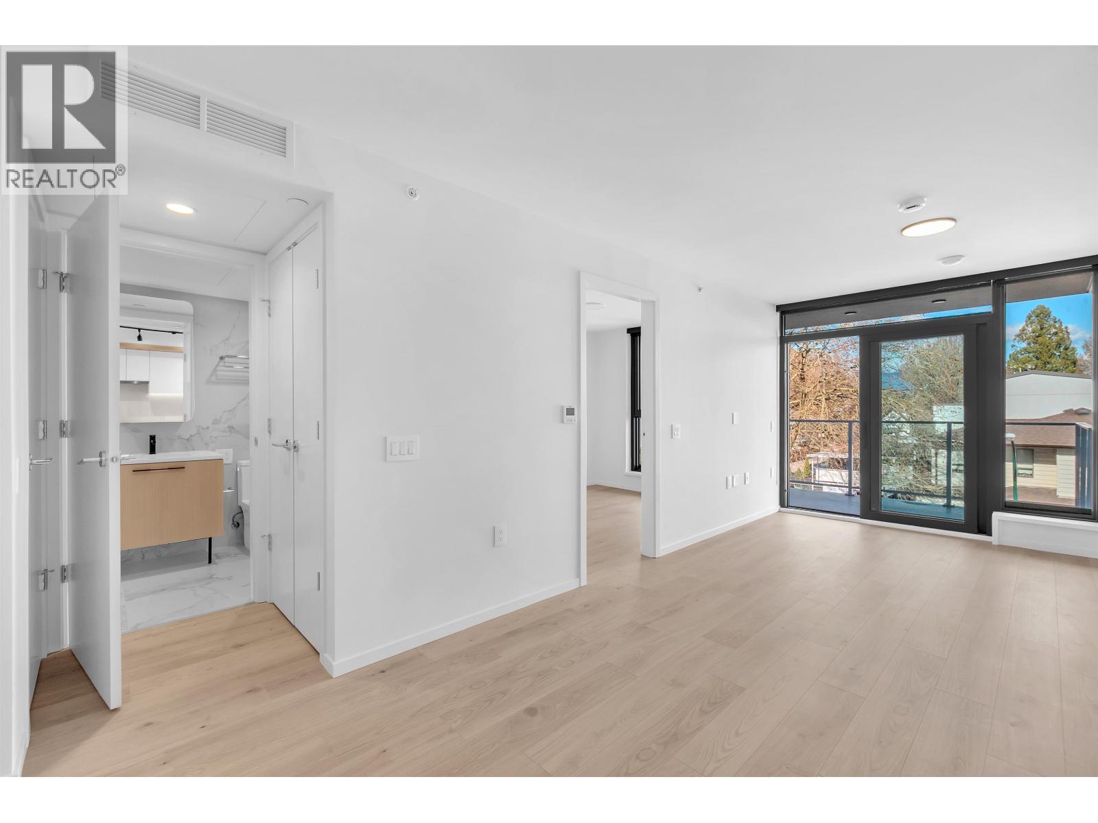 A large, empty room with a sliding glass door leading to a view of trees and a house.