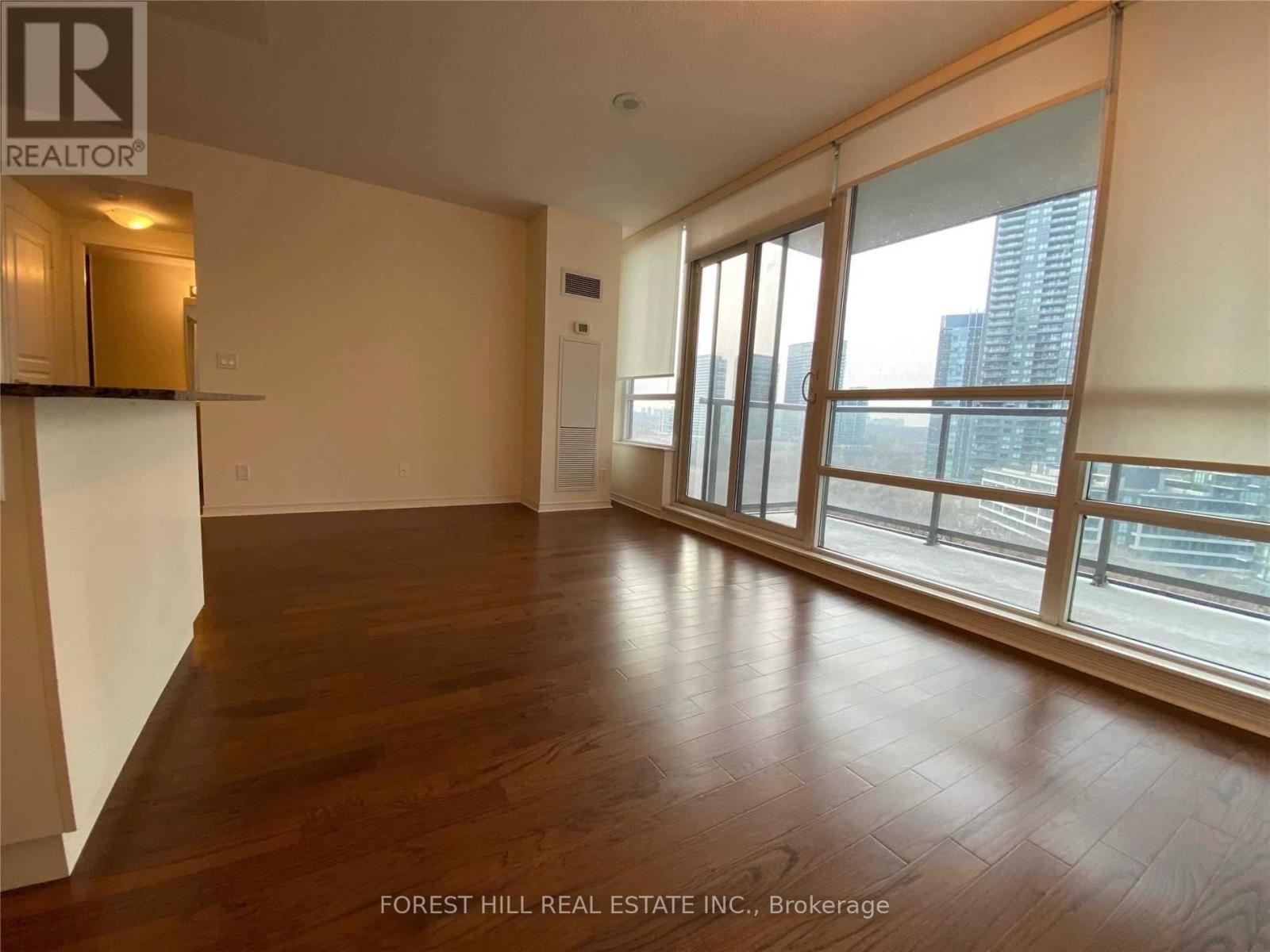 A spacious room with wooden floors and large windows overlooking a cityscape.