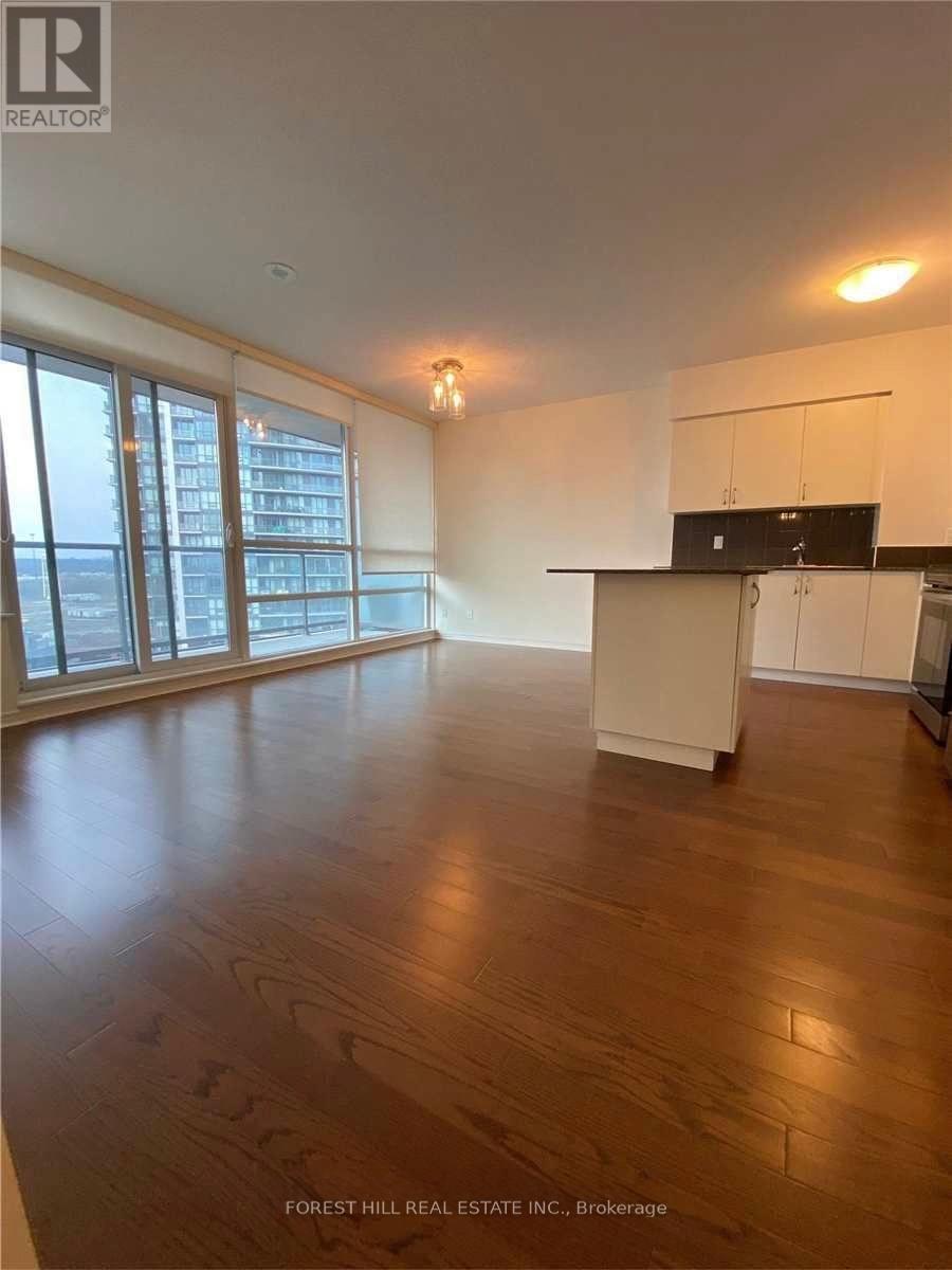 A spacious living room with wooden floors and a kitchen area in the background.