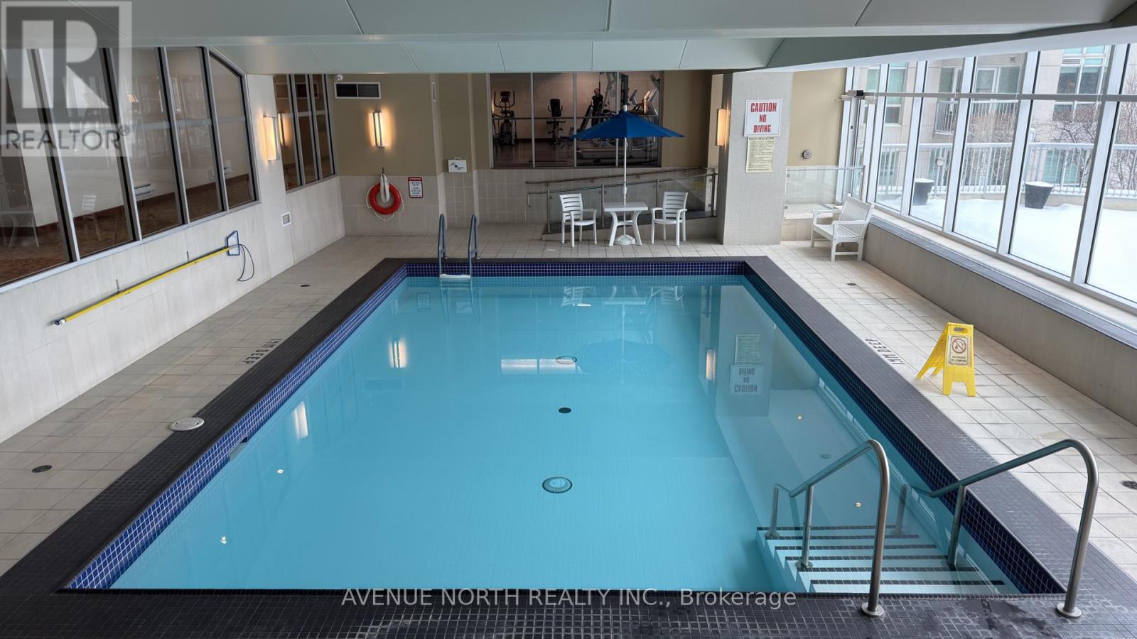 A large indoor swimming pool with a diving board and ladders.