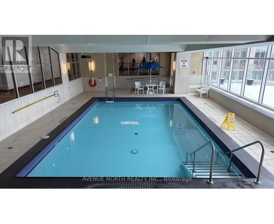 A large indoor swimming pool with a diving board and ladders.